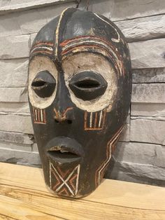 an african mask is sitting on a wooden shelf in front of a brick wall and wood planks