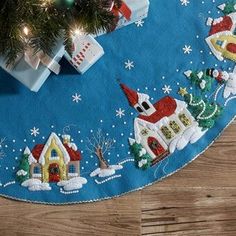 a blue christmas tree skirt with houses and trees on the bottom, surrounded by presents