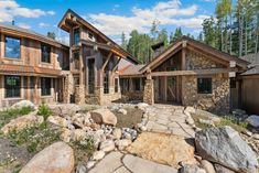 a large stone and wood house with lots of windows on the front, along with rocks and grass