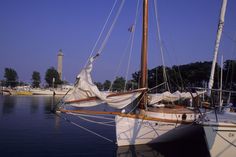 the sailboat is docked at the dock in the water near other boats and trees