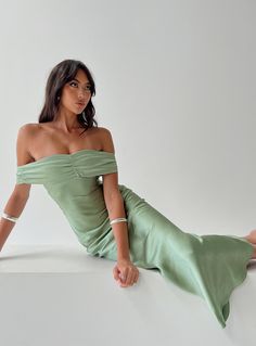 a woman in a green dress sitting on the ground with her legs crossed and one leg up