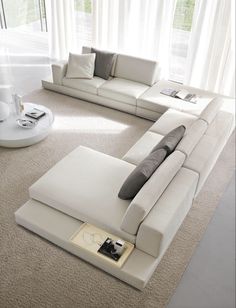 a large white sectional sofa sitting on top of a carpeted floor next to a window