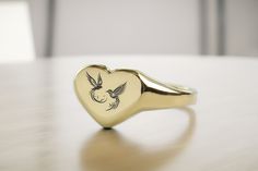 Discover the romance of our Heart Shaped Gold Signet Ring, featuring an exquisite birds engraving that symbolizes love and unity. This beautifully designed ring is a tribute to love in all its forms, capturing the essence of deep affection and companionship. The heart-shaped signet serves as a canvas for the tender scene of two birds, making it an ideal piece for engagements, anniversaries, or as a declaration of love. Made from premium gold for a lasting shine, it's a piece that will be cherish Symbolic Heart Shaped Wedding Rings, Symbolic Heart-shaped Wedding Ring, Heirloom Engraved Heart Ring For Promise, Heirloom Engraved Heart Promise Ring, Elegant Engraved Signet Ring For Valentine's Day, Heirloom Heart-shaped Engraved Ring As Gift, Heirloom Heart-shaped Engraved Ring For Gift, Heart-shaped Engraved Rings For Weddings, Heart Shaped Engraved Rings For Wedding