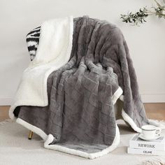 a gray and white blanket sitting on top of a wooden floor next to a cup