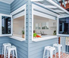 an outdoor kitchen with white stools on the wooden floor and blue painted house exterior