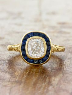 an antique diamond and blue sapphire ring on a wooden surface, with the center stone surrounded by gold filigrees