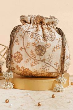 "Colour: Cream Embroidered front and back. Dimensions (LxB): 9.5\" x 9\" (24 cm x 23 cm) Handle drop: 5\" (13 cm) Material : Embroidered poly silk, poly satin lining, woven golden thread drawstrings and handle, scallop lace and pearl tassels." Bollywood Style Handwork Bags For Reception, Bollywood Style Bags With Handwork For Reception, Embroidered Rectangular Potli Bag For Reception, Traditional Potli Bag With Dori Work For Reception, Festival Reception Potli Bag With Zari Work, Festive Potli Bag With Gold Embroidery, Zari Work Potli Bag For Festivals And Reception, Festive Gold Embroidery Potli Bag, Gold Potli Bag With Dori Work For Reception