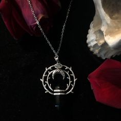 a necklace with an arrow in the center on a black surface next to a rose