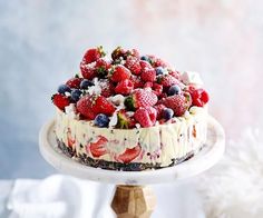 a cake topped with berries and whipped cream on top of a wooden stand next to a white cloth