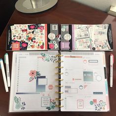 an open planner book sitting on top of a wooden table next to pens and markers