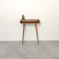 a small wooden table with a glass vase on it's top sitting in front of a white wall