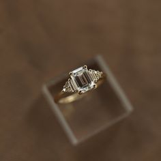 an engagement ring with three diamonds on it sitting on top of a wooden table in front of a brown background