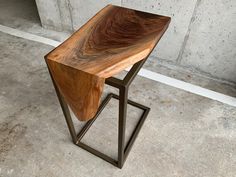 a wooden table sitting on top of a metal stand in front of a cement wall