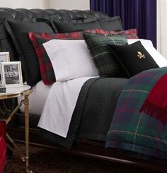 a bed with plaid sheets and pillows in a bedroom next to a table with pictures on it