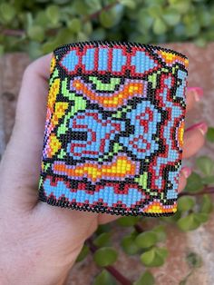 a hand holding a colorful beaded square object in it's left hand,