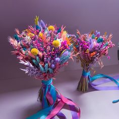 two vases filled with colorful flowers on top of a white table next to a ribbon