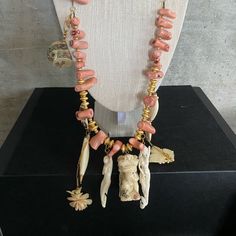 The Necklace Has Coral Beads That Vary In Shape And Alternate With Gold Disk Beads. It Has Pendants That Hang From It (Pictured). Some Are Carved Sirens Or Horns, Some Are Flowers, And Some Are Traditional Figures. Pink Artisan Beaded Jewelry, Artisan Pink Jewelry With Round Beads, Traditional Pink Gemstone Beads Necklaces, Artisan Pink Beaded Necklace, Traditional Pink Gemstone Bead Necklace, Traditional Pink Gemstone Beads Necklace, Traditional Pink Necklaces With Gemstone Beads, Traditional Pink Necklace With Gemstone Beads, Pink Single Strand Bohemian Beaded Necklaces