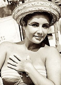 a woman wearing a straw hat sitting in a chair with her hands on her chest