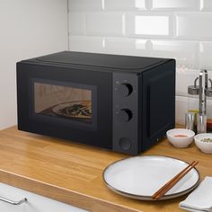 a black microwave oven sitting on top of a counter next to plates and chopsticks