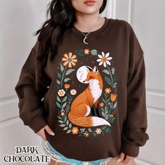 Wrap yourself in nature's beauty with our charming fox and floral moonlit sweatshirt. This design features a majestic fox sitting gracefully amidst an array of blooming flowers, with a serene moonlit background. Ideal for animal lovers and nature enthusiasts, this cozy sweatshirt is perfect for casual outings, cozy nights, or a unique gift. Made from high-quality materials, it offers comfort and durability, ensuring you stay warm and stylish. Whether you're exploring the outdoors or lounging at Fox Cardigan, Fox Hoodies, Fox Sweatshirts, Fox Shirt Pink, Wild Fox Boutique Crewneck, Fox Sweater, Graphic Sweaters, Nature Inspired Design, Cozy Sweatshirts