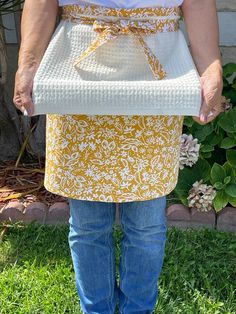 a woman is wearing an apron and has her hands in the back pocket, while standing on grass