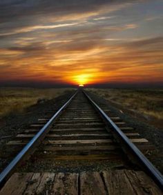 the sun is setting over an empty train track