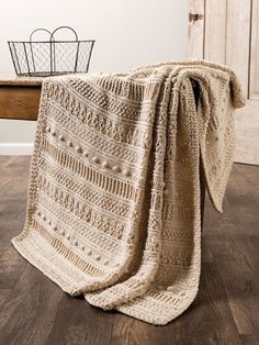 a crocheted blanket draped over a wooden table with a basket on top of it