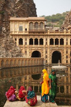 two women in colorful sari are standing near the water