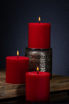 three red candles sitting next to each other on top of a wooden table in front of a dark background