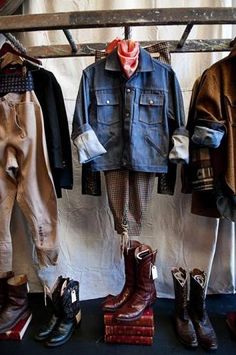 several different types of clothing hanging on a clothes rack with shoes and boots in front of them