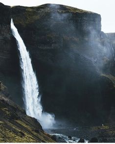 a large waterfall is coming out of the side of a mountain with people standing on it