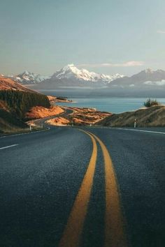 an empty road in the middle of nowhere with mountains in the background and snow capped peaks