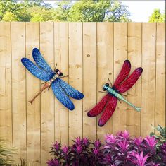 two metal dragon sculptures sitting on top of a wooden fence next to purple and green plants