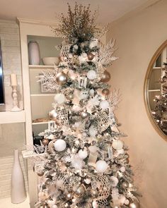 a silver and white christmas tree in a living room with ornaments on the top,