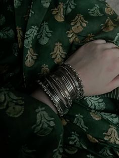 a close up of a person wearing bracelets and a green shirt with gold flowers on it