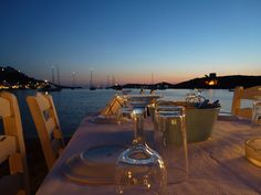 the table is set with plates and wine glasses on it, overlooking the water at night