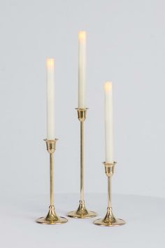 three brass candlesticks with one lit and the other turned off, on a white background