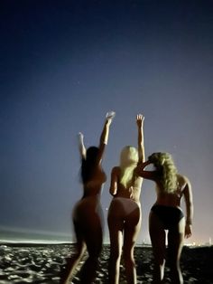 three women standing on the beach with their arms in the air