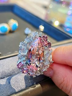 a person is holding a fancy ring with pink and white diamonds on it's side