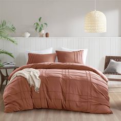 a bed with an orange comforter and pillows in a room next to a plant