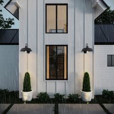 a white house with potted plants in front of it and rain falling on the ground