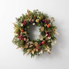 a christmas wreath hanging on the wall with pine cones, berries and other greenery