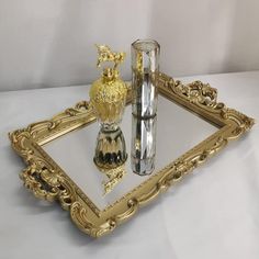 an ornate gold tray with two vases and a bottle on it, sitting next to each other