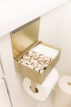 an open toilet paper dispenser in a white bathroom with gold trim on the lid