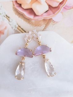 a pair of earrings sitting on top of a white marble slab next to pink flowers