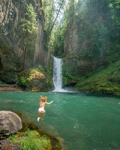 a woman jumping into the water in front of a waterfall