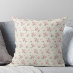 a white pillow with pink flowers on it sitting on a couch next to two pillows