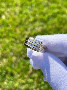 a person wearing a gold ring with white stones on it's side and green grass in the background