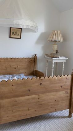 a wooden bed sitting in a bedroom next to a white table with a lamp on it