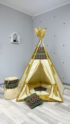 a teepee tent with pillows on the floor in front of it and a basket